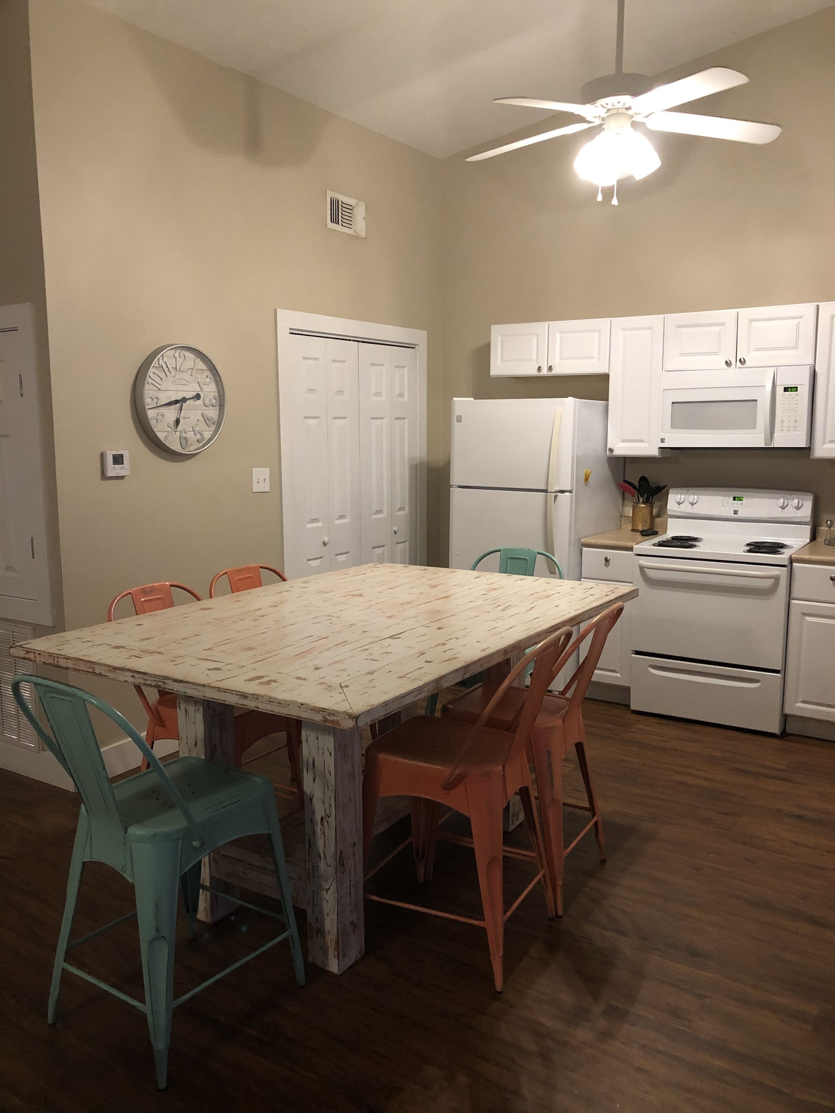 A kitchen with white cabinets, a white refrigerator, a white stove, a clock on the wall, and a ceiling fan.