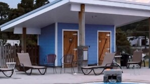 A pool area with lounge chairs and a small building with doors.