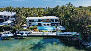 A modern house with a swimming pool, surrounded by lush greenery and palm trees. - Iconic Ted Williams Estate. Bayfront, Heated Infinity Pool & Hot Tub, Dockage. (Islamorada)