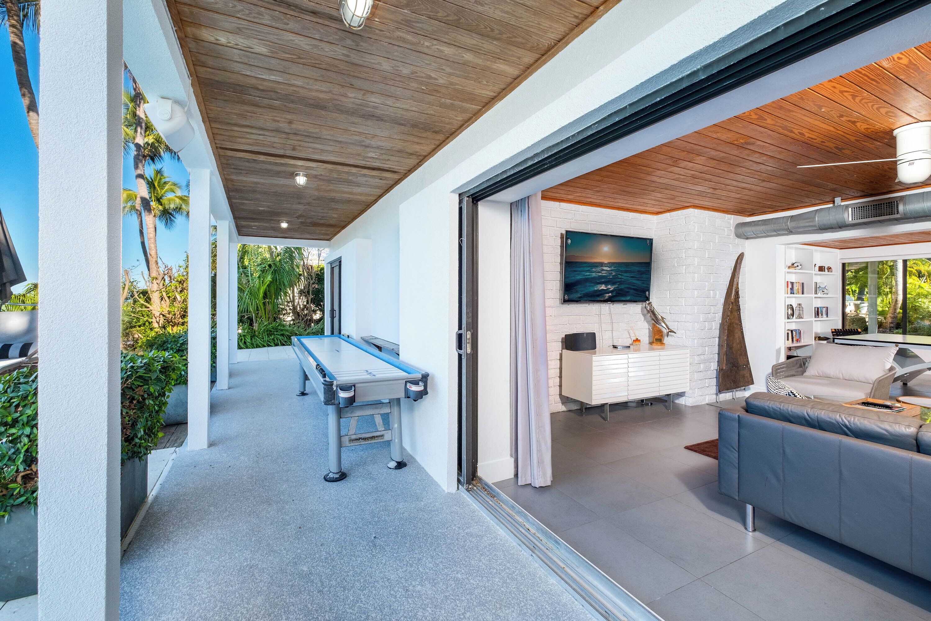 A modern living room with a pool table, a sofa, and a dining area with a white brick wall and a painting.