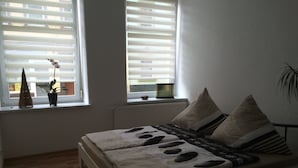 A bedroom with a bed, a window with blinds, a small plant, and a yellow rug. - Ferienwohnung Riesa (Riesa)