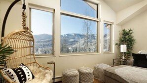 A cozy room with a large window, a hanging chair, a bed, and a small table with a lamp. - Homes (Aspen)