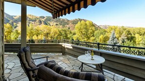 A covered outdoor seating area with a stone floor, a table with two wine glasses and a bottle, and a view of a mountainous landscape. - Homes (Aspen)