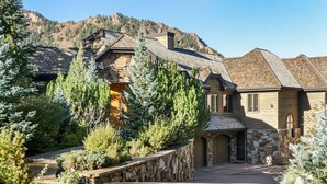 A two-story house with a stone facade, a stone entrance, and a driveway leading to a garage. - Homes (Aspen)