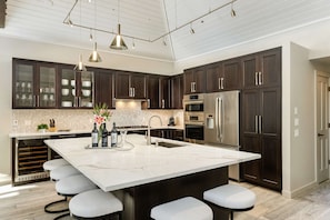 A modern kitchen with dark wood cabinets, a large island with bar stools, stainless steel appliances, and pendant lighting.
