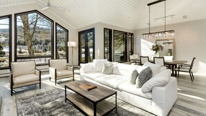 A spacious living room with a white sofa, a coffee table, and a dining area with a chandelier. - Homes (Aspen)
