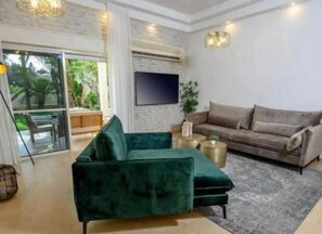 Relax in this stylish living room with a large sectional sofa, flat-screen TV, and sliding glass door leading to an outdoor area.