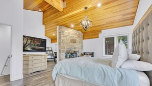 A bedroom with a large bed, wooden ceiling, stone wall, and a television on a dresser. - Modern Ski-in/Ski-out in Silver Lake. Fully Remodeled. Steps to the slopes!!! (Deer Valley)