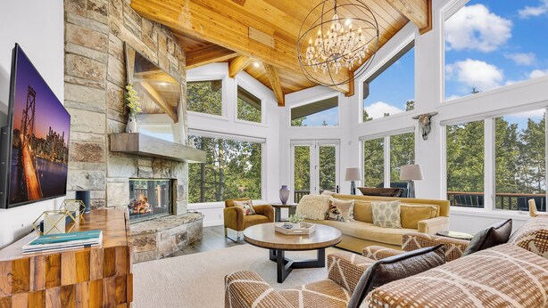 A spacious living room with a stone fireplace, large windows, and a high ceiling with exposed beams. - Modern Ski-in/Ski-out in Silver Lake. Fully Remodeled. Steps to the slopes!!! (Deer Valley)