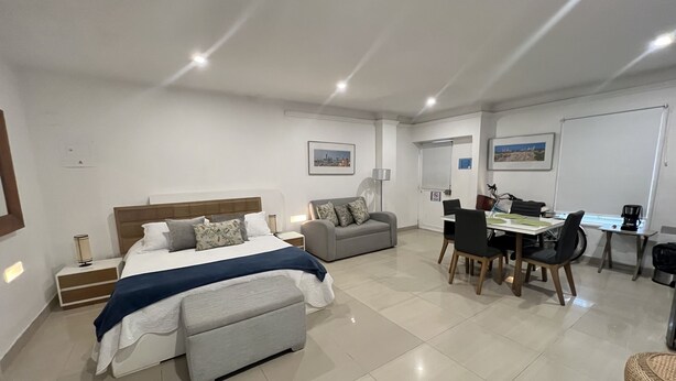 A modern hotel room with a large bed, a grey sofa, a dining table with chairs, and a wheelchair-accessible table. - BEAUTIFUL APARTMENT STUDIO IN HISTORICAL CENTER  (Cartagena)