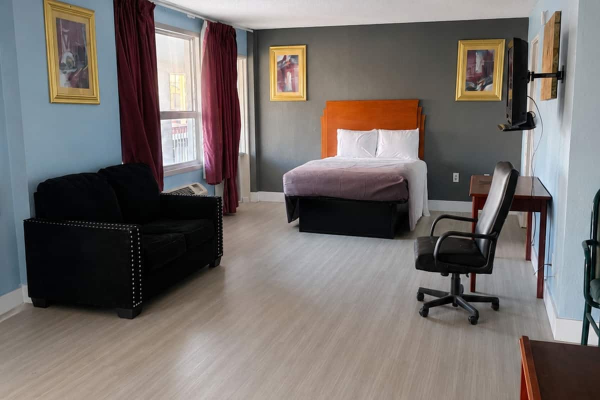 A hotel room with a bed, a black sofa, a desk, and a chair.