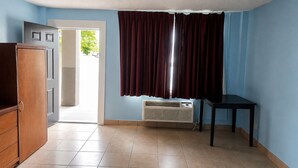 Ein Zimmer mit einer zur Außenseite führenden Tür, einem fensterbelaubten Fenster, einem Heizkörper und einem kleinen Tisch.