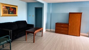 Ein Zimmer mit einer schwarzen Couch, einem Holztisch, einem Holzschrank und einem gerahmten Bild an der Wand.