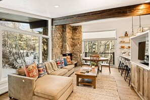 A spacious living area with a stone wall, a sofa with patterned cushions, a coffee table, and a dining area with chairs and a table. - Shadowbrook Condos by iTrip Aspen Snowmass (Snowmass Village)