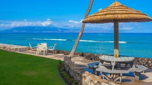 A beachside lounge with a thatched umbrella, lounge chairs, and a stone wall.