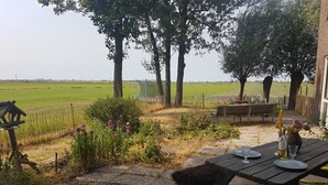 A patio with a table set for two, surrounded by a garden with a fence and trees. - 6-10 pers family home in the country, 15km from Amsterdam (Wijdewormer)