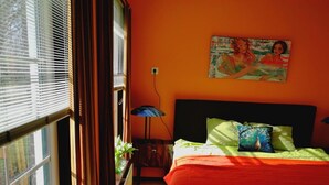 A bedroom with a large window, a bed with a red bedspread, a blue chair, a white fluffy object, a cowhide rug, and a painting on the wall. - 6-10 pers family home in the country, 15km from Amsterdam (Wijdewormer)