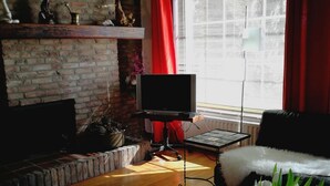A living room with a brick fireplace, a television on a stand, a sofa, and a coffee table with a vase of flowers. - 6-10 pers family home in the country, 15km from Amsterdam (Wijdewormer)