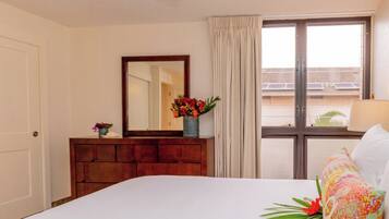 Une chambre d’hôtel avec un lit, une commode en bois, un miroir, une fenêtre avec des rideaux et une vue sur les bâtiments environnants.