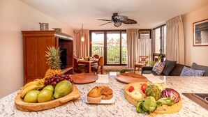 Una sala de estar con comedor, ventilador de techo y un ventanal con cortinas.