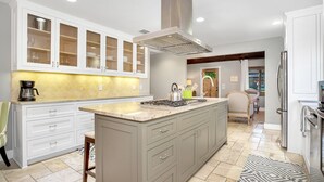 A modern kitchen with a large island, white cabinetry, and a stainless steel range hood. - Rest Haus | In Town | Hot Tub (Fredericksburg)