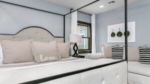 A bedroom with a bed, a bedside table, a lamp, a mirror, and a framed artwork on the wall. - Rest Haus | In Town | Hot Tub (Fredericksburg)
