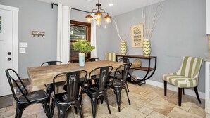 A dining area with a wooden table, black chairs, a hanging light fixture, and decorative vases on a side table. - Rest Haus | In Town | Hot Tub (Fredericksburg)