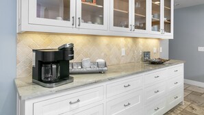 A kitchen with white cabinets, a coffee maker, and a tiled backsplash. - Rest Haus | In Town | Hot Tub (Fredericksburg)