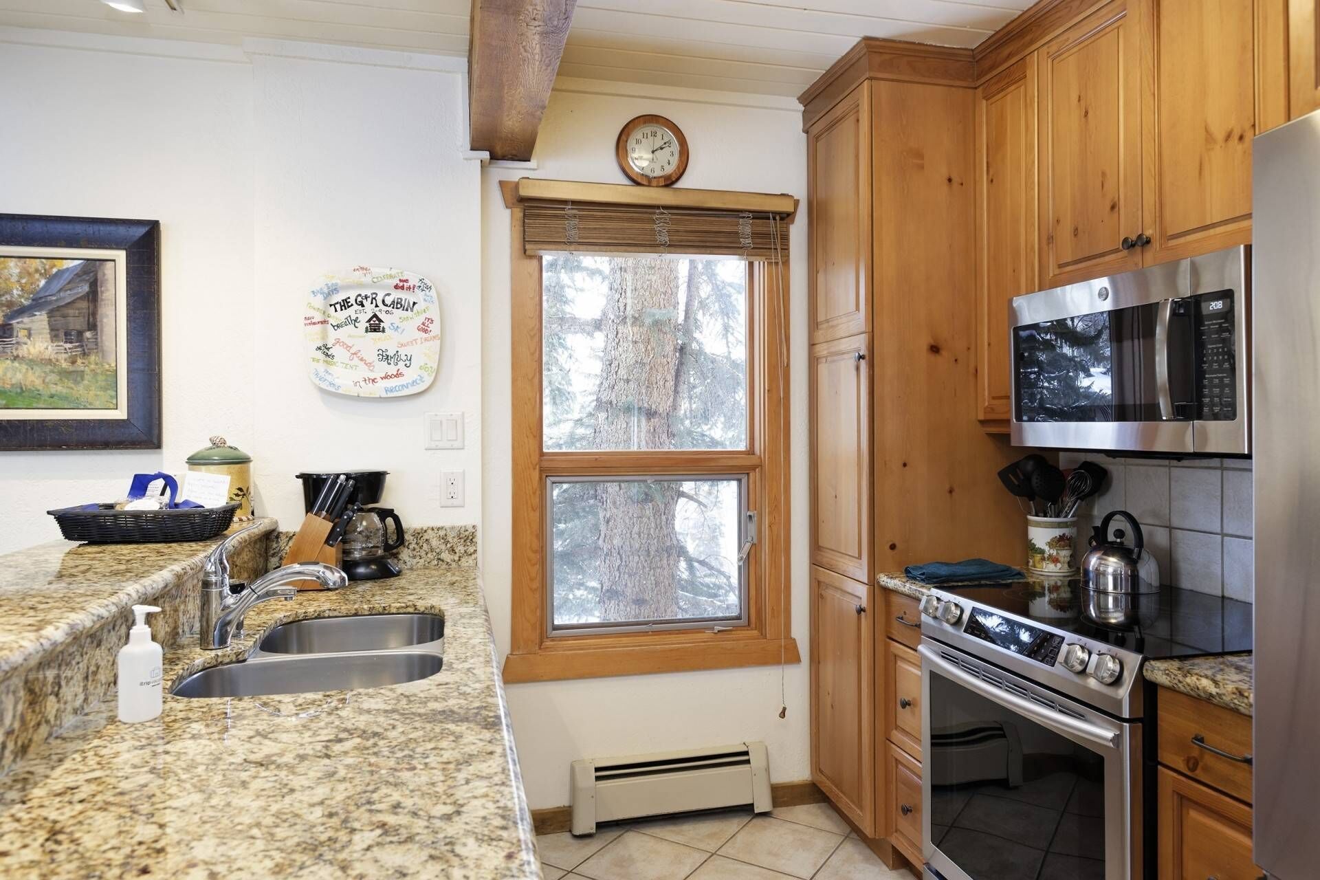 Eine Küche mit Granit-Arbeitsplatten, Holzschränken, einem Edelstahl-Kühlschrank, einer Mikrowelle, einem Backofen und einem Fenster mit Jalousien.