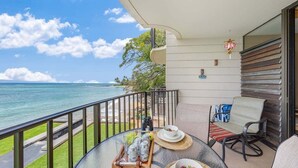 A balcony with a view of the ocean, a table with a tray of cans and glasses, and a chair with a striped cushion.