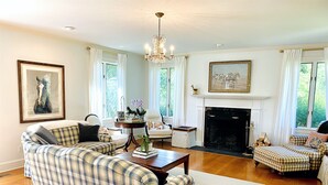 A spacious living room with a fireplace, plaid furniture, and large windows. - Tower Hill - Hilltop Country Retreat with Panoramic Views  (Millbrook)
