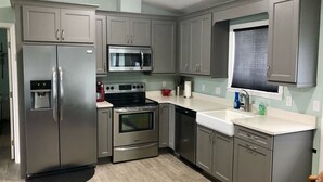 A modern kitchen with stainless steel appliances, grey cabinets, and a white countertop. - Beautiful Newly Remodeled Home on Lake Santa Fe (Waldo)