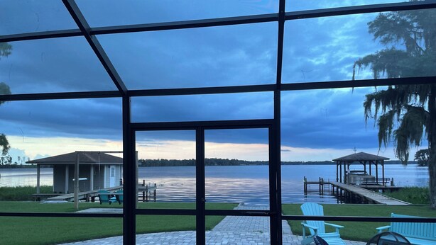 A view from a covered deck overlooking a lake with a gazebo, dock, and outdoor seating area. - Beautiful Newly Remodeled Home on Lake Santa Fe (Waldo)