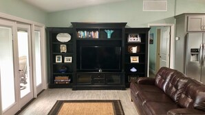 A living room with a dark entertainment center, a brown leather sofa, and a door leading to a patio. - Beautiful Newly Remodeled Home on Lake Santa Fe (Waldo)