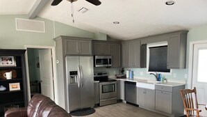 A modern kitchen with grey cabinets, stainless steel appliances, a brown leather couch, and a wooden chair. - Beautiful Newly Remodeled Home on Lake Santa Fe (Waldo)
