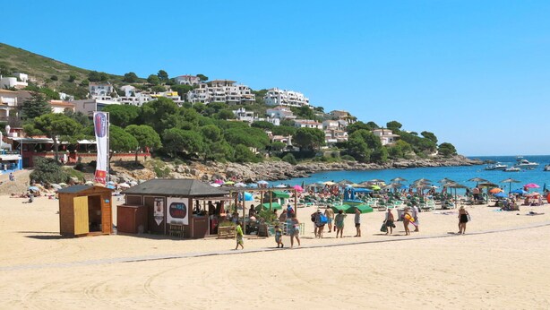 Una playa con gente, sombrillas y una pequeña construcción de madera.