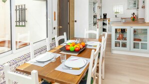 Una cocina moderna con armarios blancos, una mesa de comedor de madera dispuesta para cuatro personas y vistas al exterior.