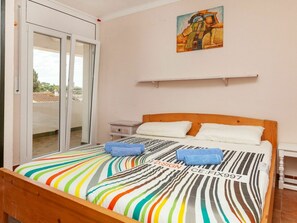 A bedroom with a bed, a nightstand, a painting, and a sliding glass door to a balcony.