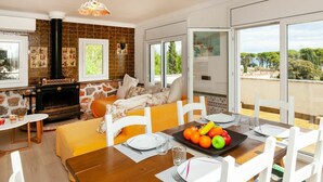 Una sala de estar acogedora con chimenea, un comedor con una mesa dispuesta para dos personas y ventanas amplias con vistas al exterior.