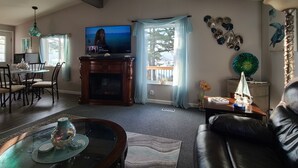 Una sala de estar con chimenea, televisión, comedor con sillas y vistas al exterior.