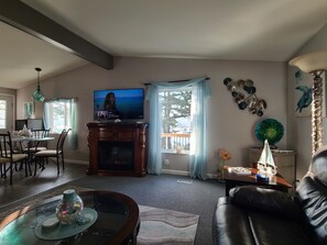 A living room with a fireplace, a television, a dining area with chairs, and a view of the outdoors.