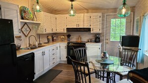 Una cocina con armarios blancos, estufa, lavabo y comedor con mesa y sillas.