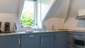 Une cuisine moderne avec des meubles gris, un four en acier inoxydable et une fenêtre donnant sur un paysage verdoyant.