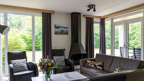 Un salon moderne doté d’une cheminée, de sièges confortables et de grandes fenêtres offrant une vue sur la verdure.