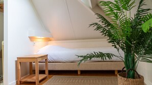 Une chambre avec un plafond en pente, un lit, une table de chevet, une lampe et une plante en pot.