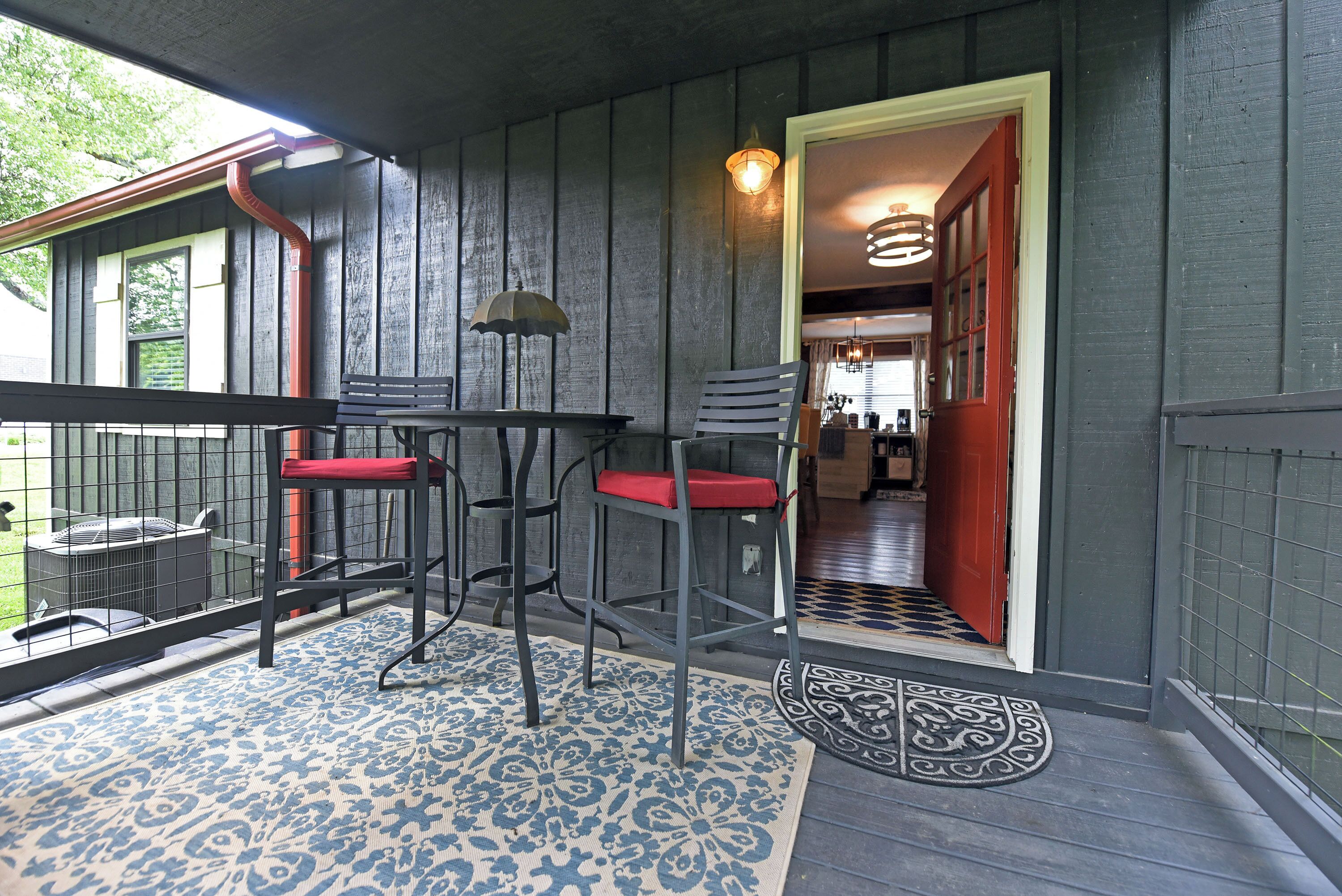 Un porche cubierto con una mesa y dos sillas, una puerta que da al interior y un tapete estampado.