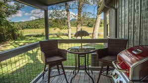 Een overdekt terras buiten met rieten stoelen, een glazen tafel en een barbecue.