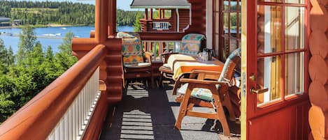 A log cabin with a balcony overlooking a lake, furnished with chairs and a table.
