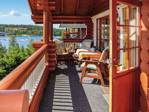 A log cabin with a balcony overlooking a lake, furnished with chairs and a table.