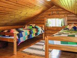 Une chambre mansardée chaleureuse avec deux lits en bois, une fenêtre avec des rideaux et un plafond en pente.